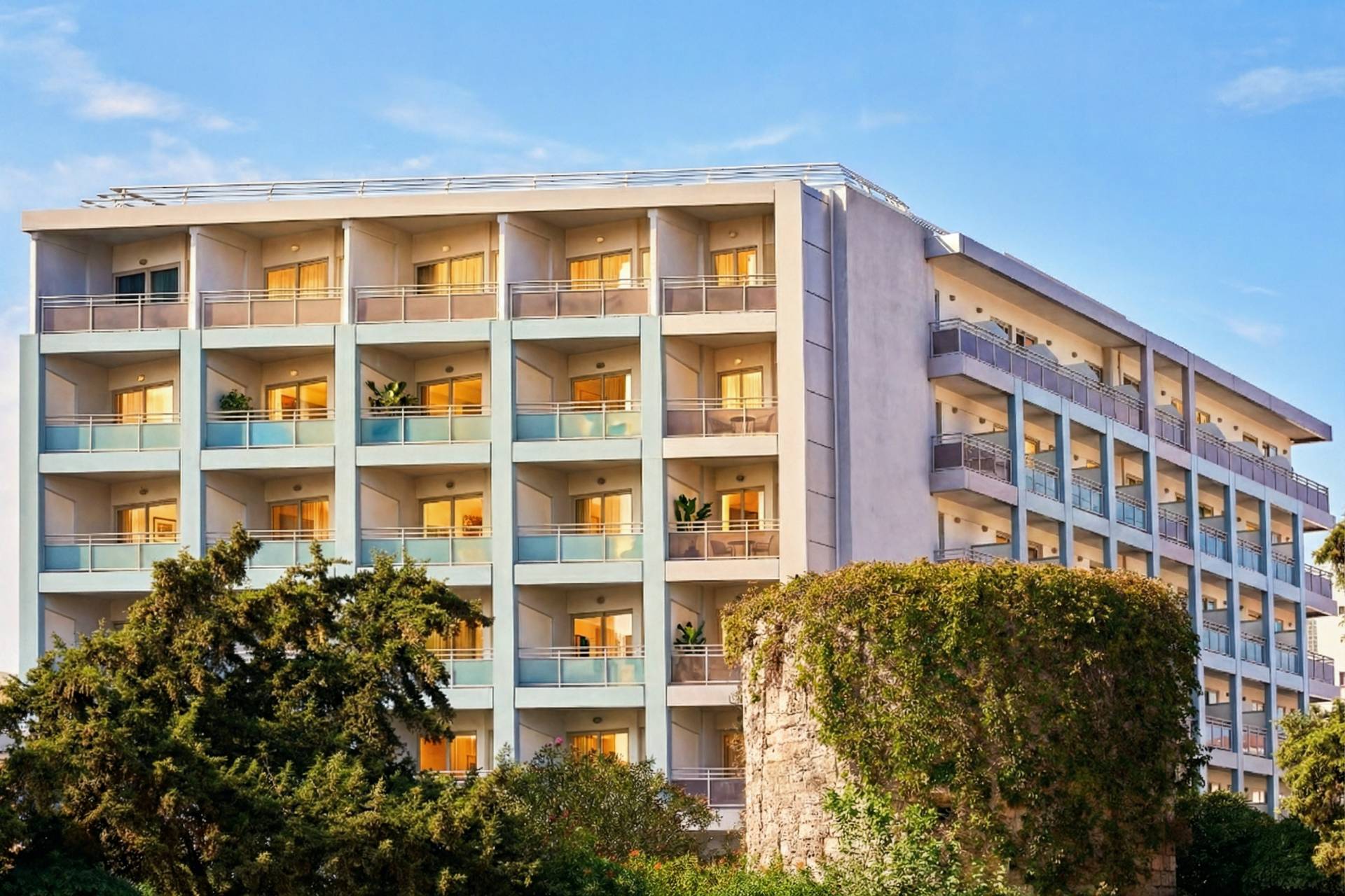 
Εξωτερική όψη του Aquamare City & Beach Hotel με φωτισμένα μπαλκόνια και πράσινο στην πόλη της Ρόδου